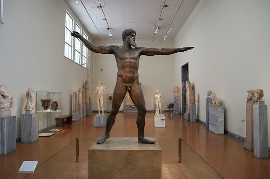 Artemision Bronze statue depicting either Zeus or Poseidon, with a muscular body, standing in a powerful pose, holding a missing object in his right hand.