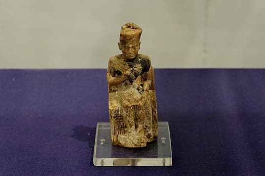 A small statue made of stone depicting King Cheops of the 4th Ancient Egyptian Dynasty sitting on a throne, exhibited in the Egyptian Museum in Cairo, Egypt.